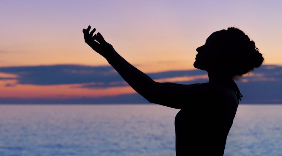 A woman is standing at twilight with her arms out stretched