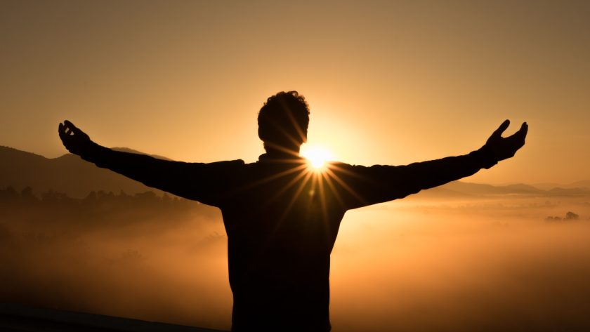 A person with arms out stretched standing on a hill at sunset