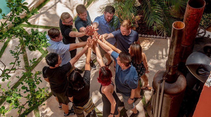 A larg group of young adults are standing in a circle, hands all in lime to give a cheer.