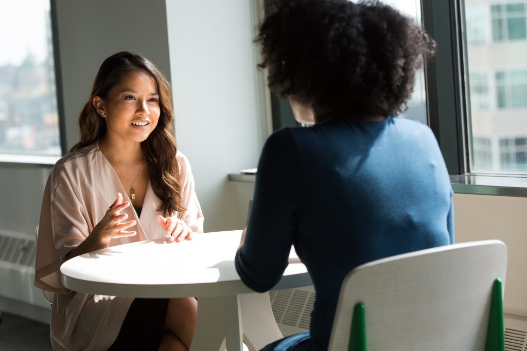 2 women, 1 white and 1 African American are sitting at a table and talking