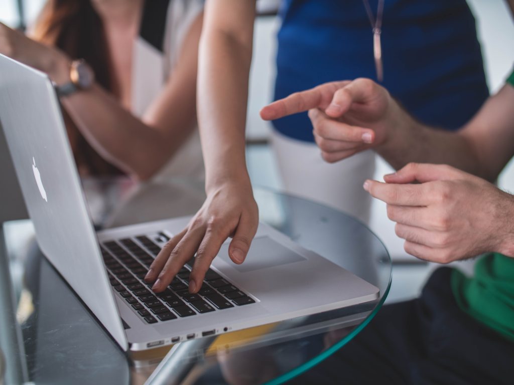 People are standing above a laptop computer and posting