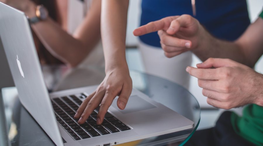 People are standing above a laptop computer and posting