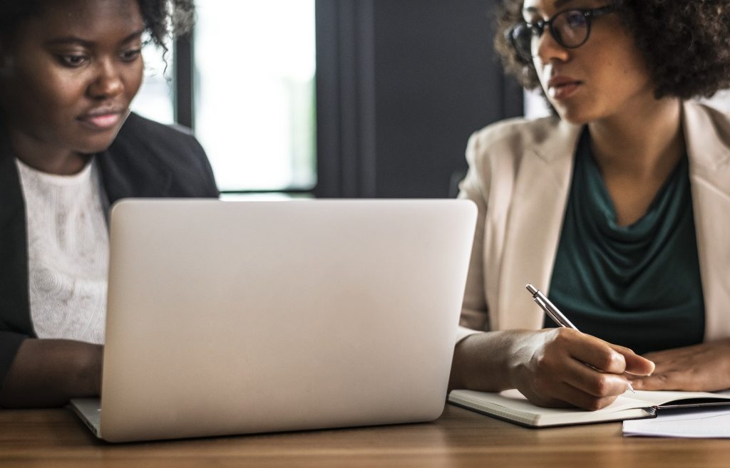 2 African American woman are sitting in front of a computer talking.