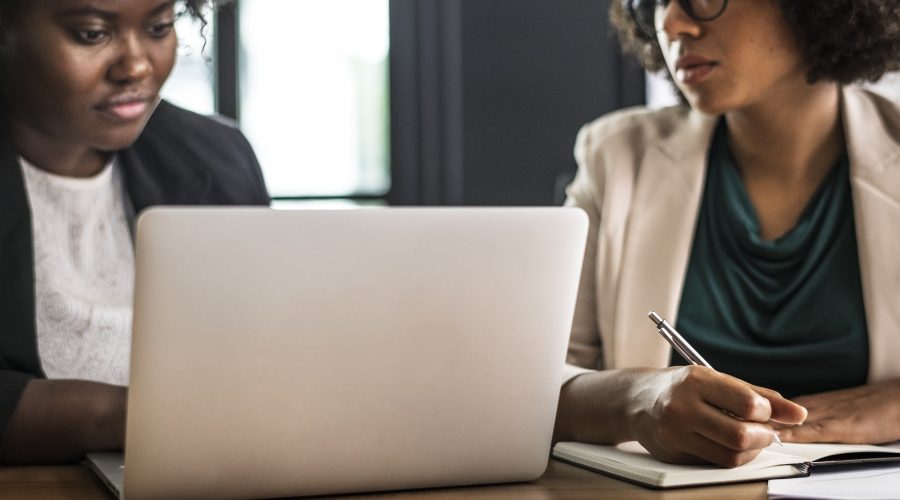 2 African American woman are sitting in front of a computer talking.