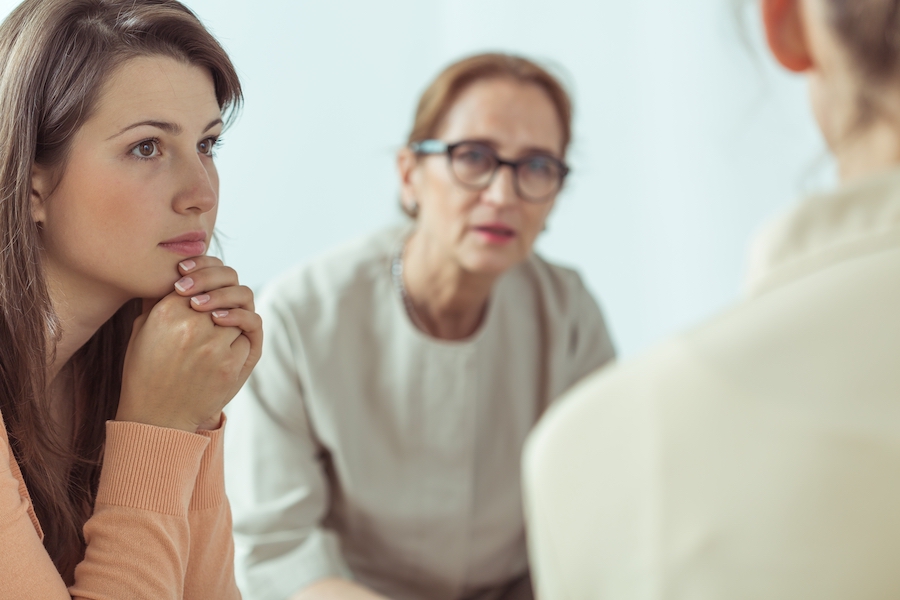 2 woman are sitting talking to a third person.