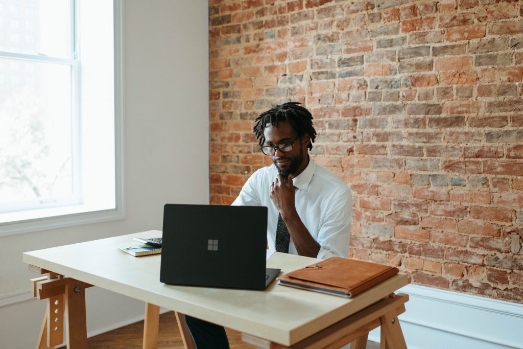 An African American man is sitting at a table with a laptop computer