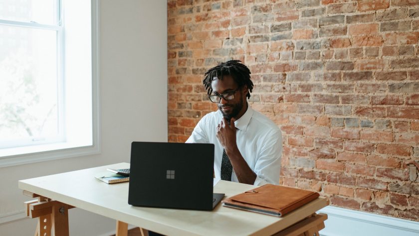 An African American man is sitting at a table with a laptop computer