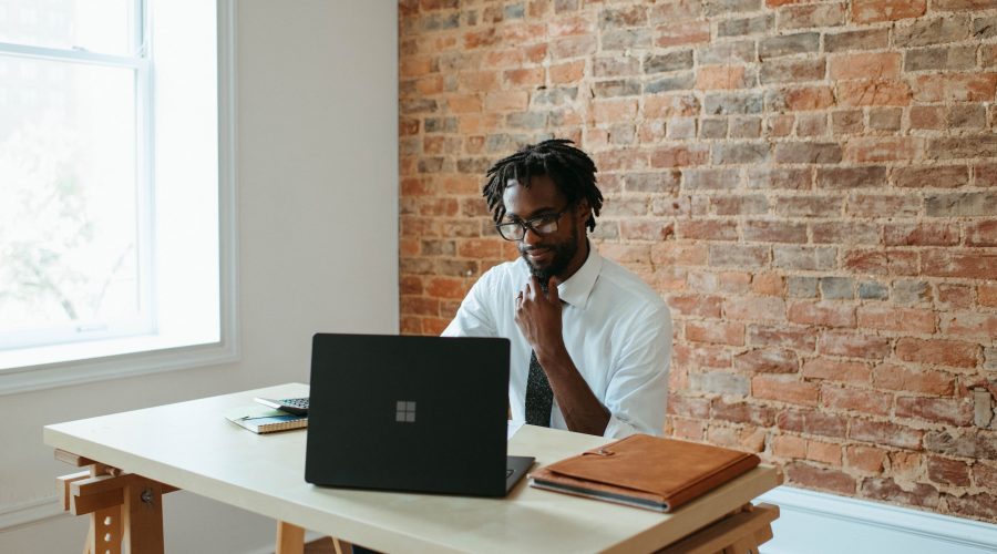 An African American man is sitting at a table with a laptop computer