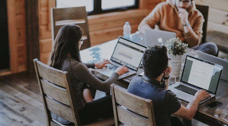 A small group of men and women are sitting at a table with computers