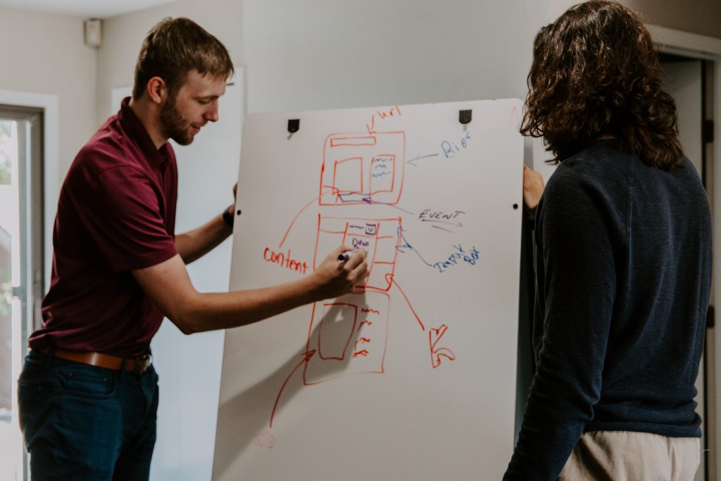 A man and a woman are standing at a whiteboard and writing on it