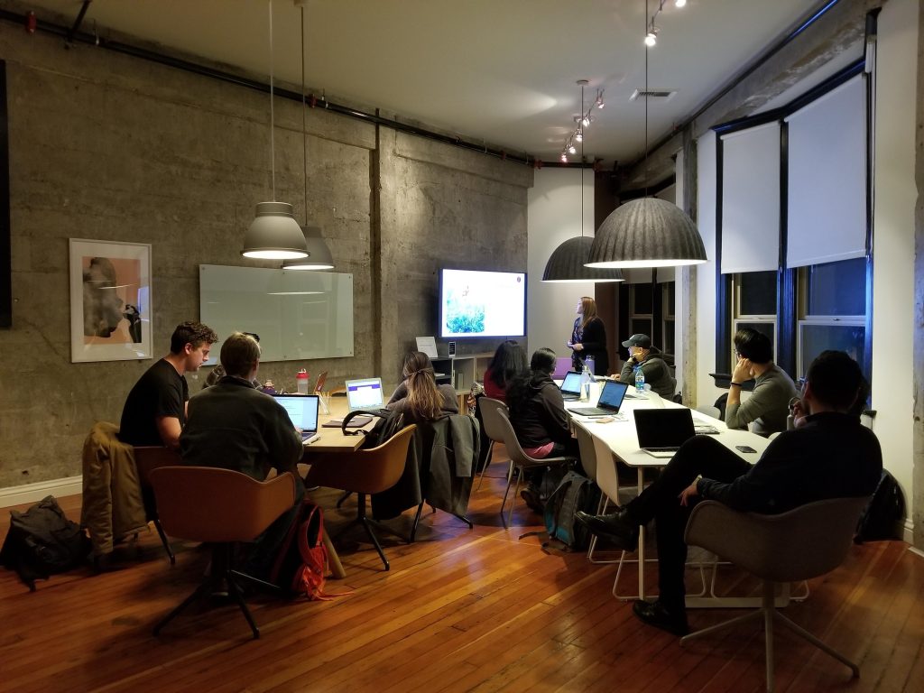 A groupmof men and woman are sitting around a table working on their laptop computers