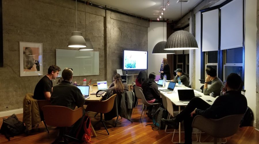 A groupmof men and woman are sitting around a table working on their laptop computers