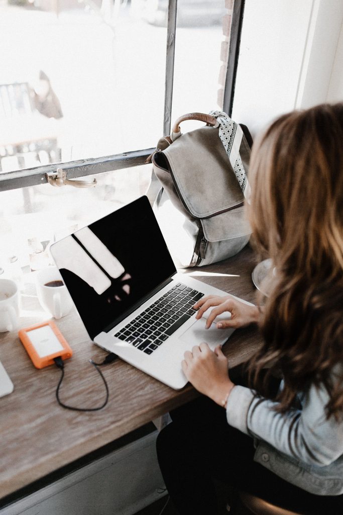 A woman is sitting at a desk typing on her laptop computer