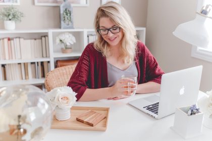 A woman is sitting at her desk, with an open laptop computer and phone