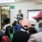 A woman is standing in front of a classroom with adults and talking