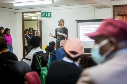 A woman is standing in front of a classroom with adults and talking