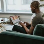 An African American man is sitting on his laptop