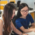 2 Girls are sitting at a desk and talking