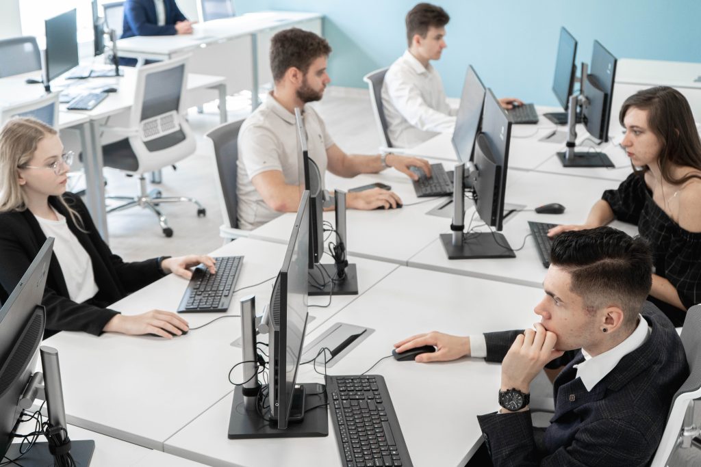A group of men and women are sitting at a large desk with computers