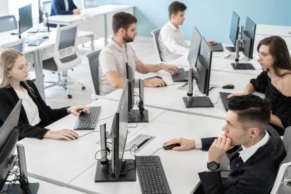 A group of men and women are sitting at a large desk with computers