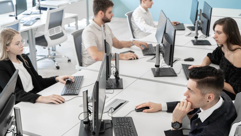 A group of men and women are sitting at a large desk with computers