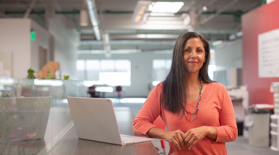 A business woman is standing at a table with her laptop computer open.