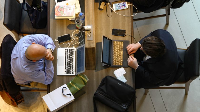 2 People are sitting a desk working on their laptop computers