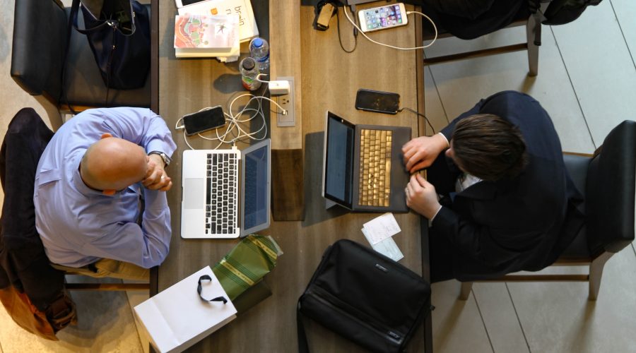 2 People are sitting a desk working on their laptop computers