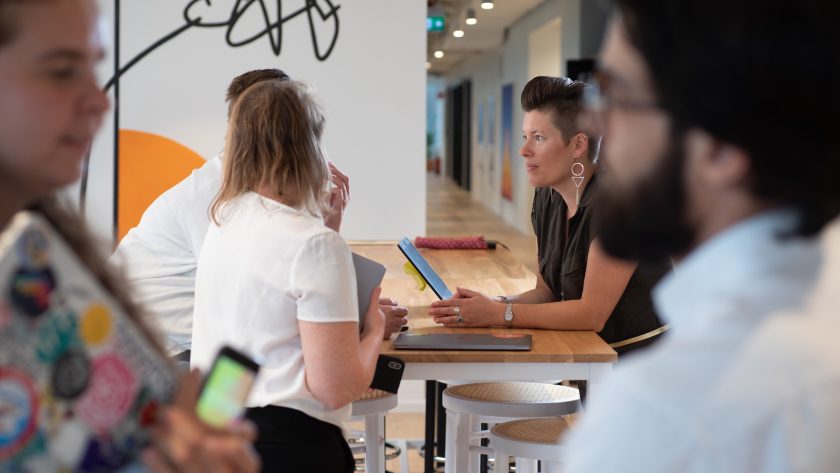 A group mod men and woman are standing around a table and talking