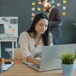 A woman is sitting at her computer laptop