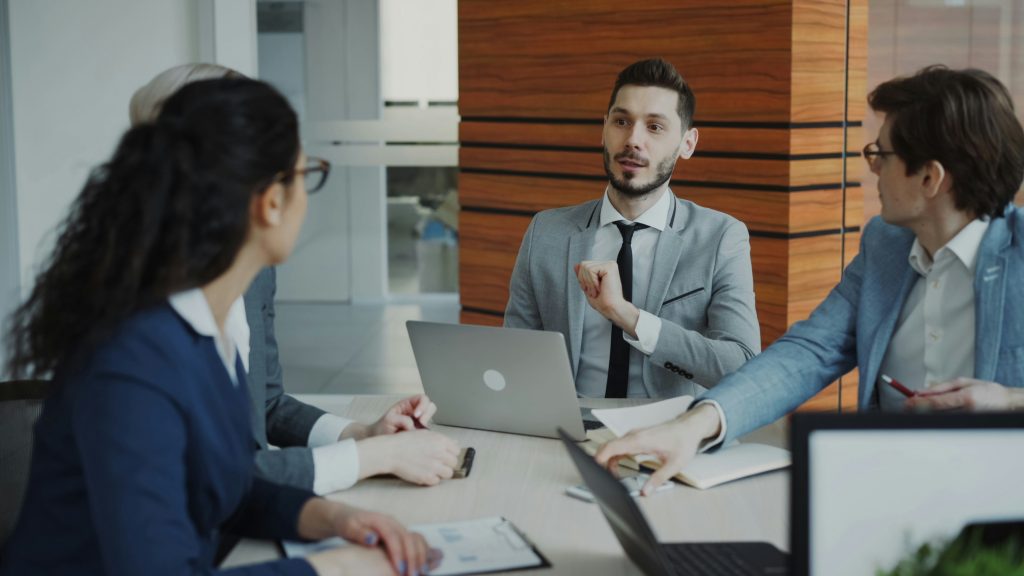 A group of business people are sitting around a desk talking