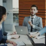 A group of business people are sitting around a desk talking