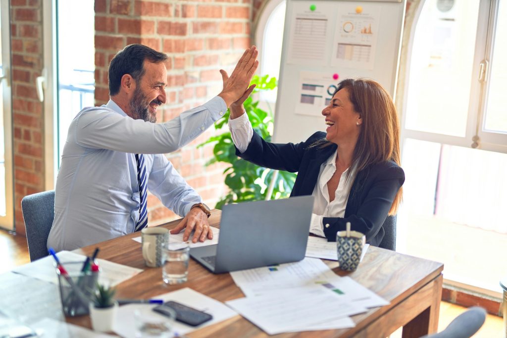 A business man and woman are sitting and giving each other the high-five