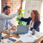 A business man and woman are sitting and giving each other the high-five
